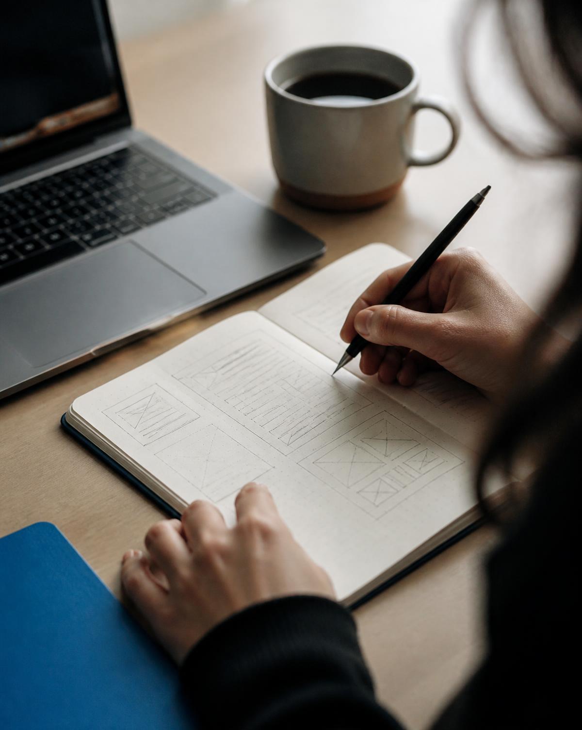 A Lynxio designer sketching interface wireframes in a notebook beside a laptop